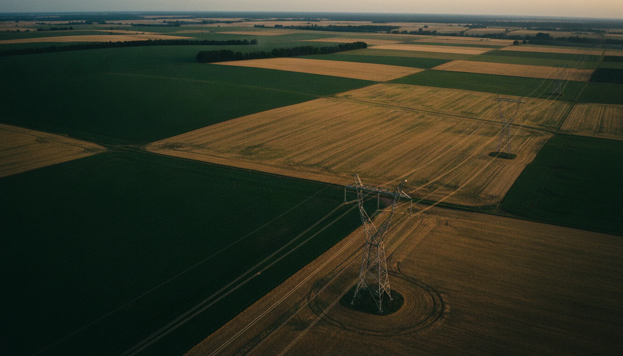 Aerial view of transmission pylons crossing green and gold farmland at low sun